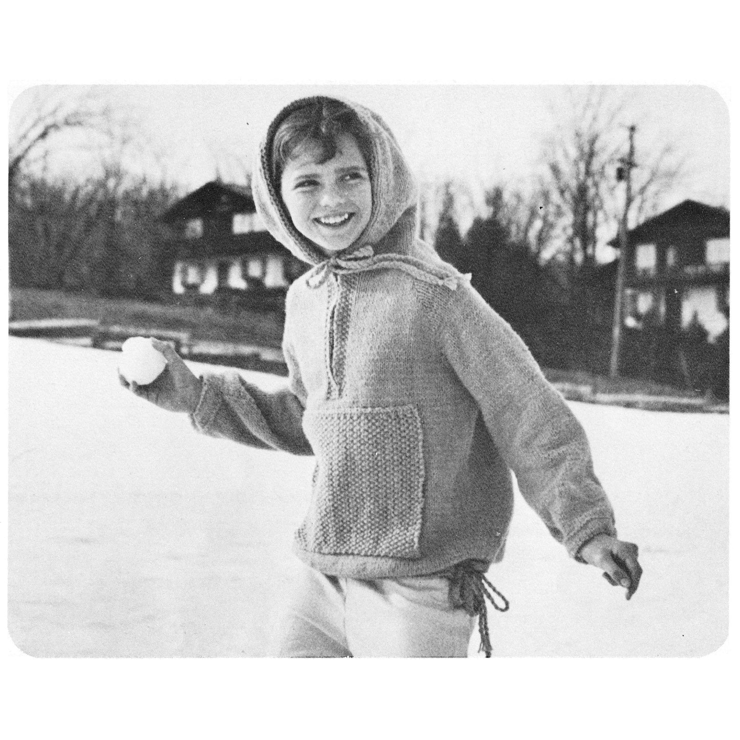 Black and white photo of a child in a knitted sweater holding a snowball outdoors.