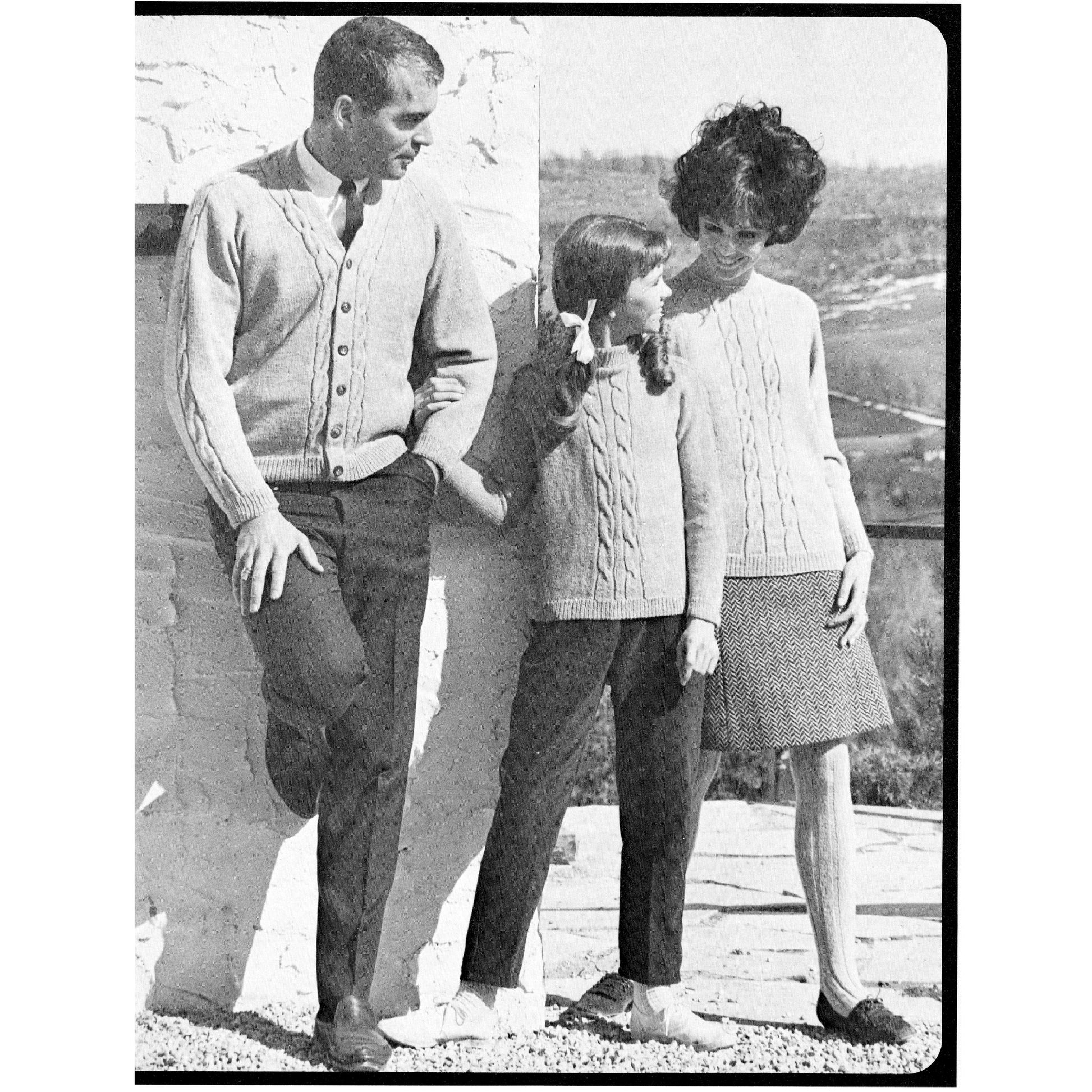 Black and white photo of three people wearing knitted sweaters outdoors.