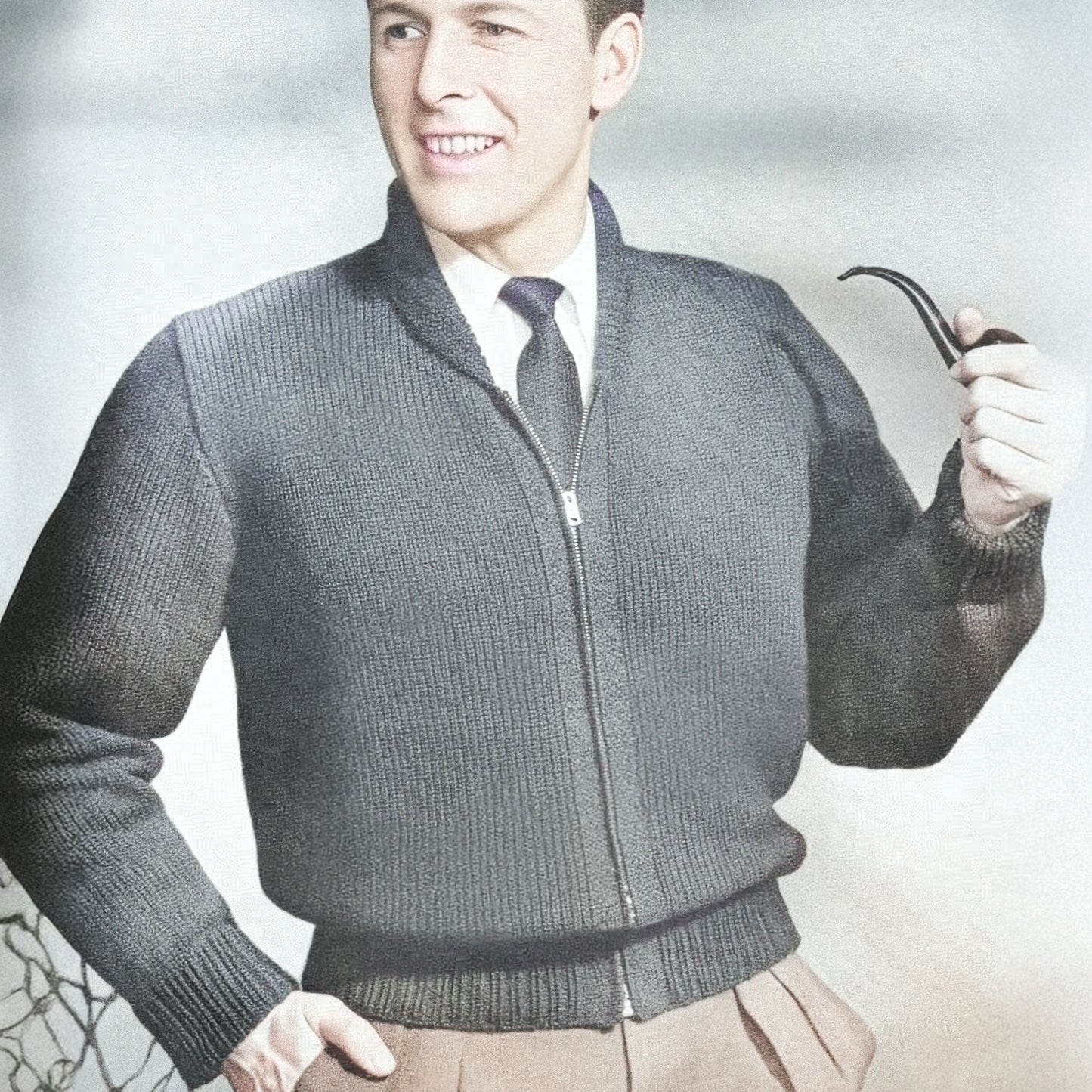 Man wearing a dark gray knitted sweater with a zipper, holding a pipe against a light background.